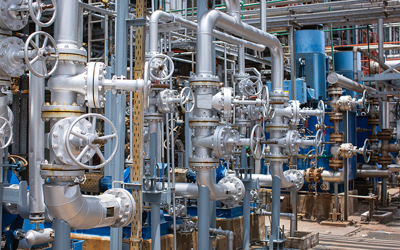 A dense industrial network of silver pipes and manual valves at an outdoor facility.
